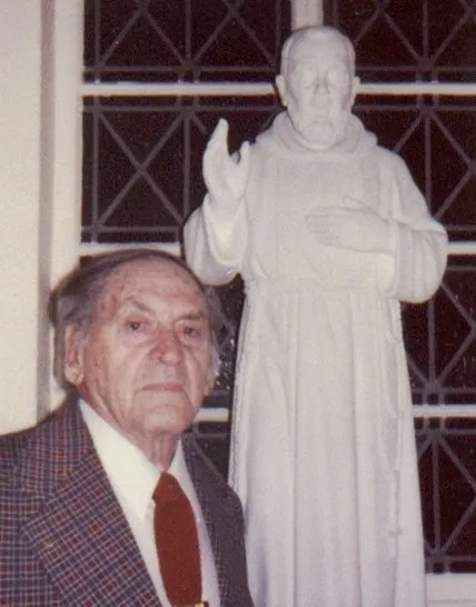 Elderly man standing beside religious statue.