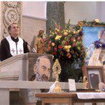 A priest is standing at the pulpit in front of pictures.