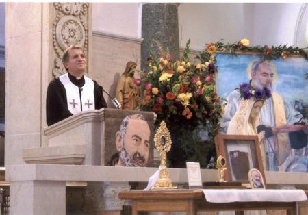 A priest is standing at the pulpit in front of pictures.