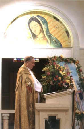 A man in a robe standing next to a flower arrangement.