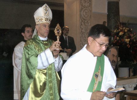 A priest is holding up his cross while standing next to another man.