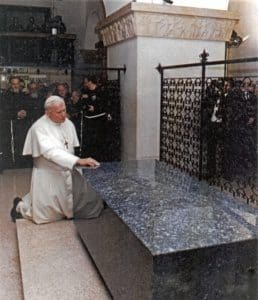 A man kneeling down next to a large stone bench.