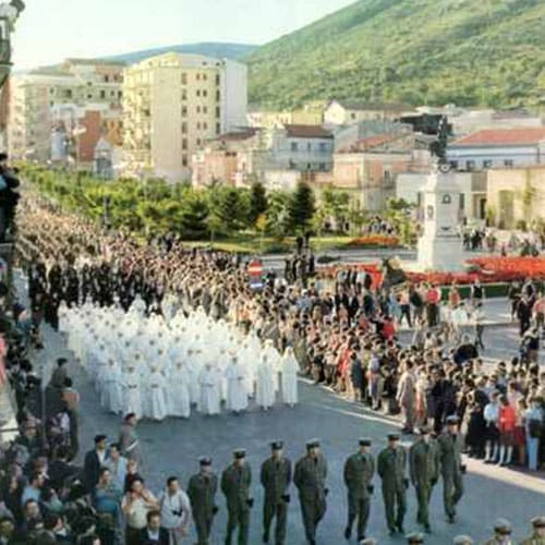 A parade of men in white suits and green pants.