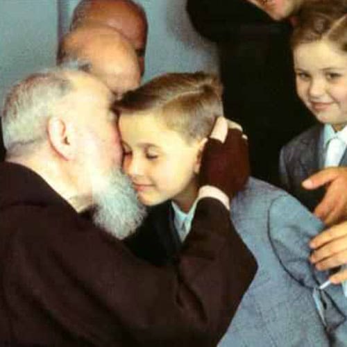A man with a beard and glasses is kissing a boy 's head.