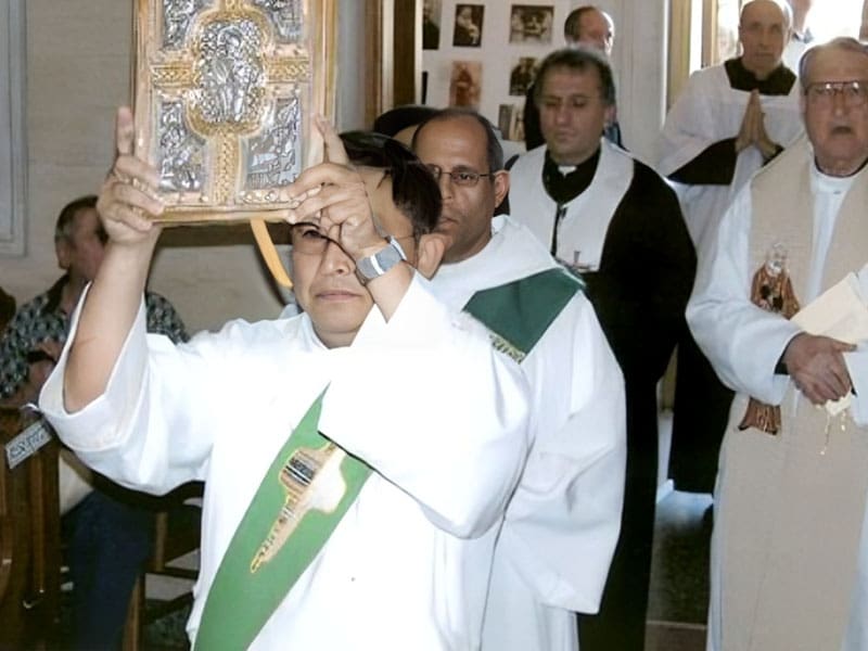 A man in white and green holding up a cross.