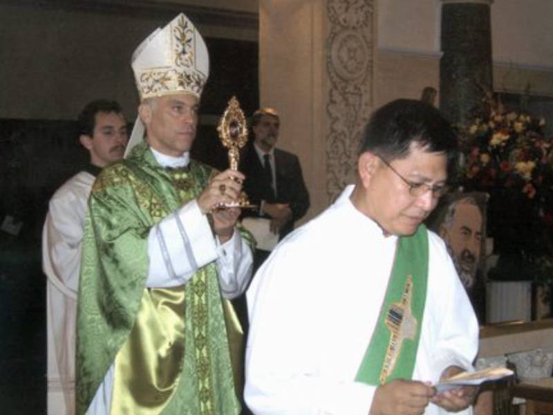 A priest is holding a cross while standing next to another person.