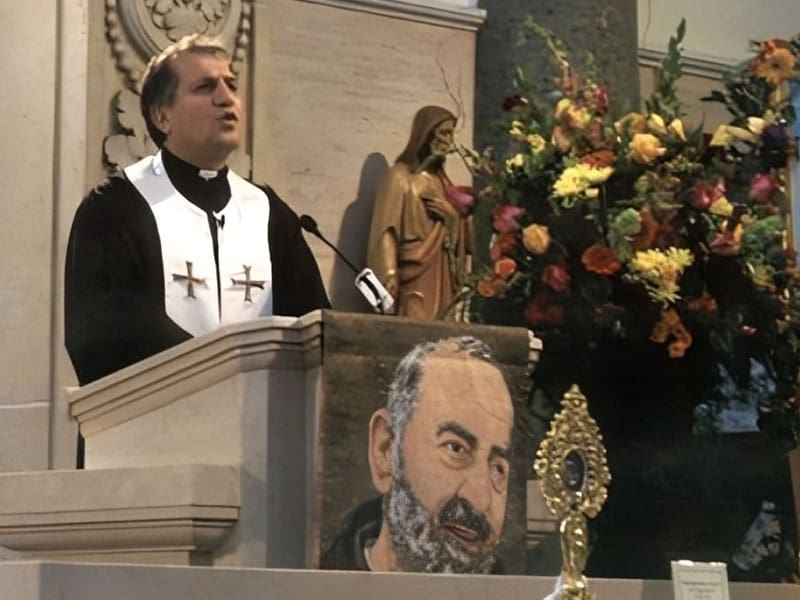 A priest is giving a sermon in front of a painting.