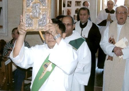 A priest holding up a cross while standing next to other priests.