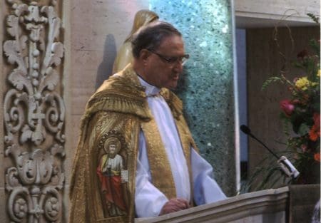 A man in a gold robe and glasses standing at the podium.