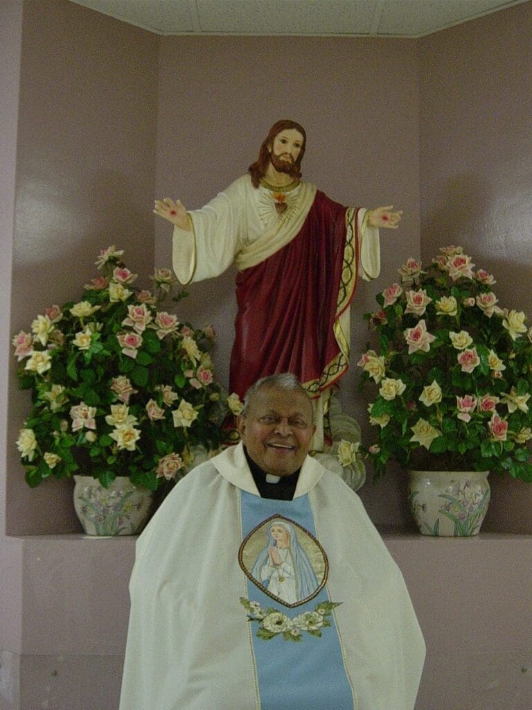 Smiling priest in front of religious statue.