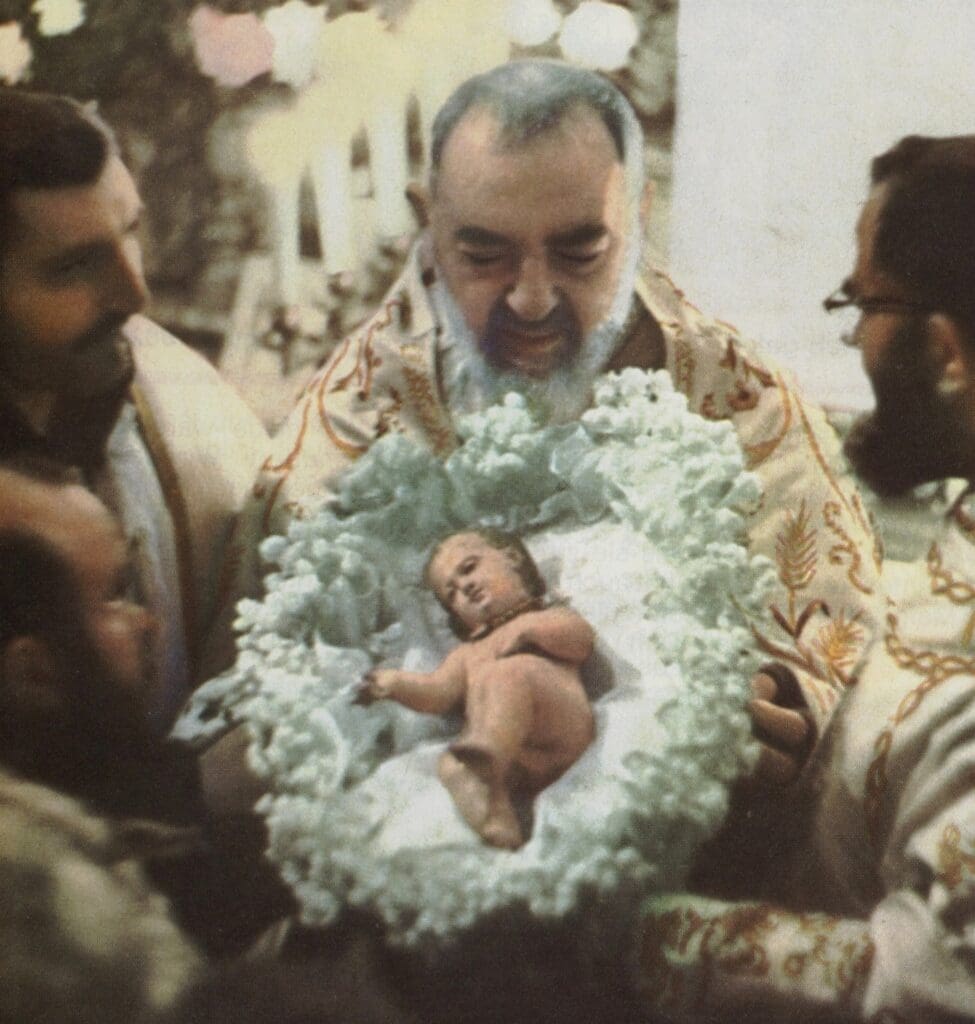 Priest holding a baby figure surrounded by congregation.