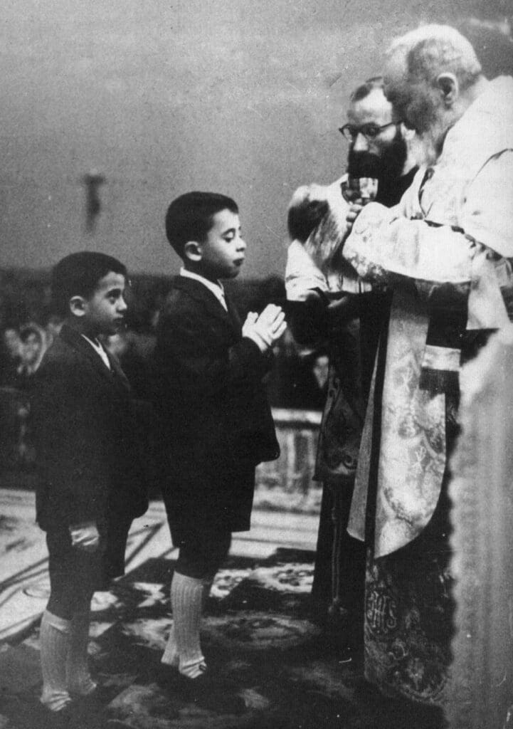 Priest blessing two young boys in church.