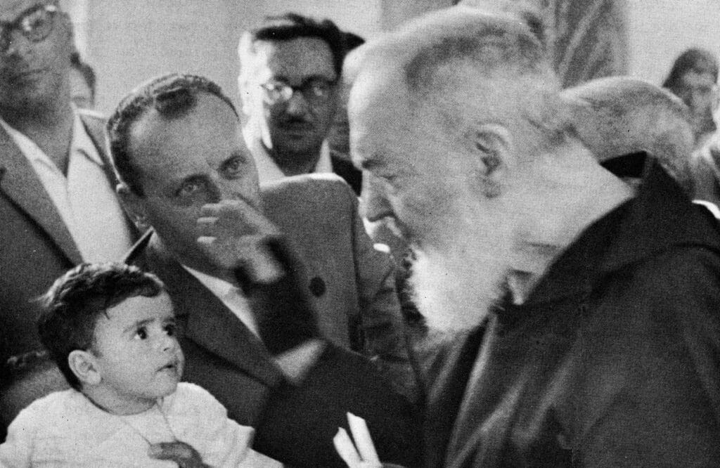 Elderly man blessing a child, surrounded by onlookers.